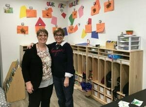 Two women pose for a photo in a classroom